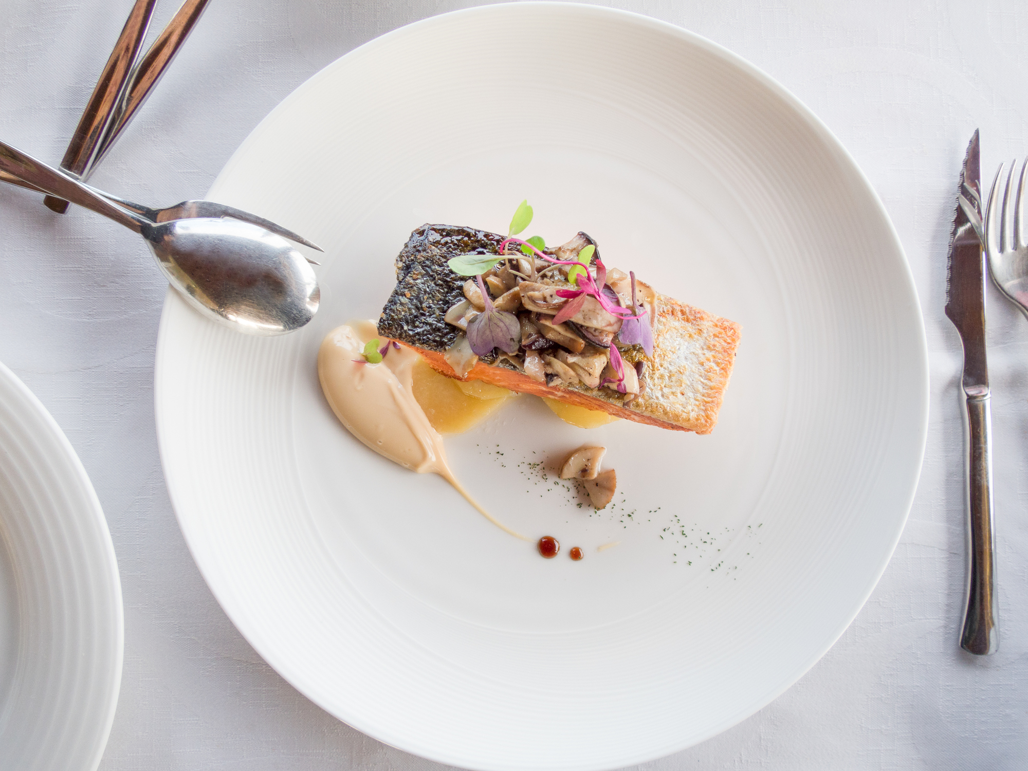 Round plate of salmon with potatoes, mushrooms and coloured leaves on a table in the Lavandin restaurant at Château Les Oliviers de Salettes.